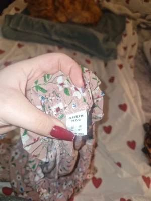 Blommig rosa kortkjol från Shein Teen - Söt rosa kortkjol från Shein Teen med blommigt mönster i vitt, blått och grönt. Kjolen har en elastisk midja och är gjord i ett lätt syntetmaterial som känns skönt mot huden. Perfekt för dig som gillar färgglada och romantiska plagg.