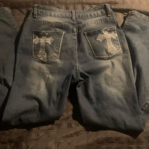 Blå jeans med broderade kors - Snygga blå jeans med unika broderade kors på bakfickorna. Perfekta för dig som vill ha en cool och annorlunda stil. Köpta begagnat så vet inte vilket märke! Skriv om ni har funderingar! Tryck på köp nu knappen🥰🥰