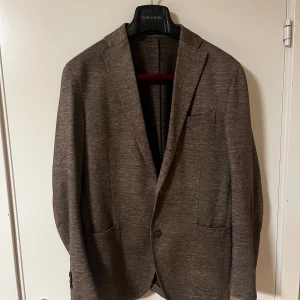 Boglioli kavaj - Säljer en stilren brun kavaj från Boglioli i storlek 46. Materialet är en mix av bomull och linne med lite stretch, vilket gör den både bekväm och snygg. Perfekt för dig som vill ha en avslappnad men ändå dressad look.