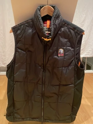 Svart dunväst från Parajumpers - Säljer en svart dunväst från Parajumpers med hög krage och dragkedja framtill. Västen har ett broderat PJS-märke på bröstet och coola detaljer som orange band i nacken. Perfekt för lager-på-lager och riktigt snygg till höst och vinter.