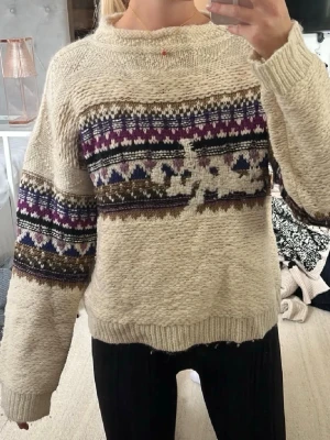 Beige stickad tröja med mönster från Isabel Marant - Säljer en beige stickad tröja med färgglatt mönster i lila, blått och brunt över bröstet och ärmarna. Tröjan har rund hals och långa ärmar, perfekt för kyliga dagar. Den är mjuk och har ribbade muddar vid ärmslut och nederkant. Fransk storlek 42 motsvarar 40.