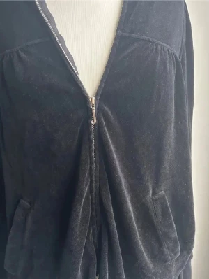 Hoodie & Svarta mjukisbyxor från Juicy Couture - Hoodie & Svarta mjukisbyxor från Juicy Couture i mjuk sammet med snörning i midjan. Klassisk rak passform och två fickor framtill. Perfekta för chill dagar och har den ikoniska Juicy Couture-loggan på insidan.