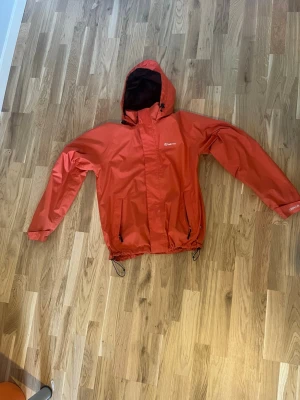 Orange regnjacka - Knappt använd regnjacka men anpassbar storlek genom gummiband på botten av jackan och vid luvan