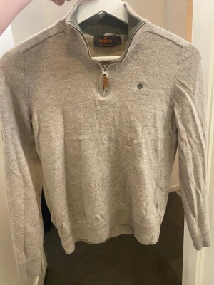 Beige merinoulltröja från Morris XS - Snygg beige tröja från Morris i 100 procent merinoull. Tröjan har half zip med läderdetalj, hög krage och logga på bröstet. Perfekt för lager-på-lager och passar till nästan allt. Långärmad och mjuk känsla storlek är L barnstolek så ungefär xs typ 160 170 . 