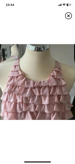 Rosa volangklänning med öppen rygg - Supersöt rosa kortklänning med flera lager volanger och öppen rygg. Klänningen är ärmlös och har en halterneck-modell som knyts i nacken. Perfekt för sommarens alla tillfällen och ger en romantisk vibe.