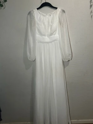 Vit långklänning  - Elegant vit långklänning från VIER i storlek S. Klänningen har transparenta långärmar, rund halsringning och ett brett, veckat midjeband som ger en snygg siluett. Materialet är lätt och flytande, perfekt för dig som gillar en romantisk och klassisk look.