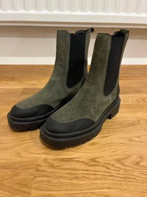 Gröna chelsea boots från Footsoul - Snygga gröna chelsea boots från Footsoul med grov svart sula och svarta elastiska paneler på sidorna. Ovandelen är i mocka och bootsen har rund tå och platt sula. Perfekta för dig som vill ha en stilren men tuff look.