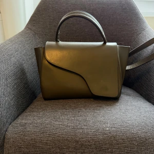 Mörkgrön handväska från ATP Atelier - Säljer en stilren mörkgrön handväska från ATP Atelier. Väskan är tillverkad i slätt skinn och har både handtag och avtagbar axelrem med metallspännen. Perfekt storlek för det viktigaste och tillverkad i Italien. Säljer då den inte kommer till användning längre och passar perfekt för alla outfits och tillfällen🥰som man ser på bilden har den några defekter i form av repor och är lite smått smutsig men om ni vill ha bilder där den är bättre avtvättad så kom privat🥰köpt för 4800kr för ca 2 år sen🥰