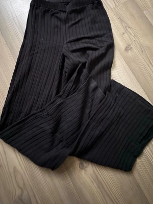 Svarta ribbade wide byxor - Säljer ett par svarta ribbade byxor med breda ben och elastisk midja. Materialet är mjukt och stretchigt, vilket gör dem riktigt sköna att ha på sig. Passformen är loose och modellen är wide, perfekt för en chill och avslappnad stil.