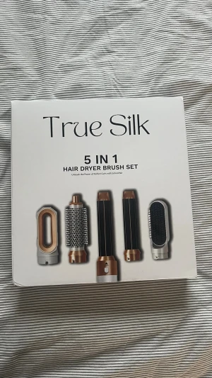 True Silk 5-i-1 hårstyler set - True Silk 5-i-1 hårstyler set med utbytbara borsthuvuden i guld och svart. Innehåller pre-styling hårtork, airstyler curler, rund volymborste och smoothing brush. Perfekt för att skapa olika frisyrer med avancerad teknik och justerbara värmeinställningar. Säljer då jag råkade få två likadana.