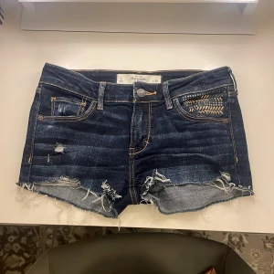Lågmidjade jeansshorts Abercrombie - Säljer ett par svin snygga mörkblå jeansshorts från Abercrombie & Fitch med slitna detaljer och råa kanter. De har små detaljer på "insidan" av ena fickan och några är av men det är inget man direkt lägger märket till. Säljer dessa för att dem är för små för mig💗💗