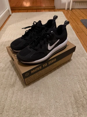 Nike Air Max Genome - Säljer ett par Nike Air Max sneakers i svart med vit swoosh och detaljer. Skorna har snörning, platt sula och synlig Air Max-dämpning. Ovandelen är i mesh och syntet för bra ventilation och komfort. Perfekt för dig som gillar stilrena och sportiga sneakers. Aldrig andvända endast testade!
