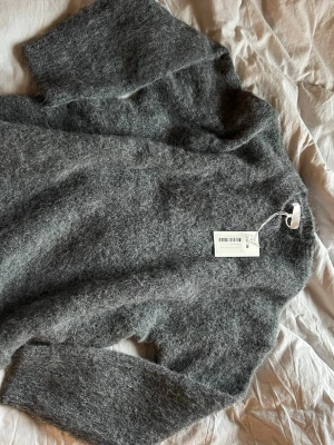 Grå oversized stickad tröja NA-KD - Mysig och fluffig grå stickad tröja från NA-KD i alpackablandning. Modellen är oversized med lång ärm och enkel design, perfekt för att hålla värmen under kyliga dagar. Färgen är mellangrå och materialet känns lyxigt och mjukt. Nypris 800