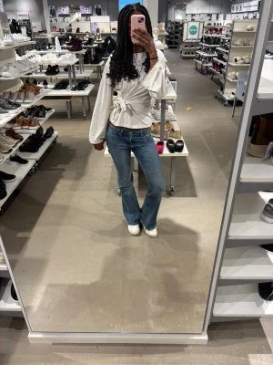 Intressekoll: Vit omlottblus med knyt - Säljer en vit omlottblus med knyt i midjan och långa, vida ärmar. Blusen har en snygg v-ringning och är gjord i ett mjukt material som känns skönt mot huden. Perfekt för dig som gillar stilrena och trendiga plagg med lite extra detalj. Den är använd max 6 ggr