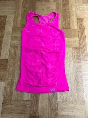 Rosa sportlinne - Säljer en snygg och sportig rosa linnetopp från Kari Traa med racerback och diskret mönster av stjärnor. Toppen är tillverkad i ett stretchigt syntetmaterial som andas och passar perfekt för träning. Logga finns tryckt längst ner på framsidan och baksidan. Storlek XS/S🩷