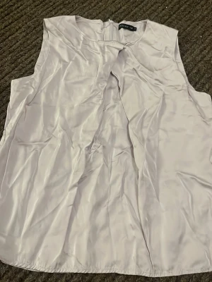 Ljuslila ärmlös blus från Stockh LM - Säljer en stilren ljuslila blus från Stockh LM i storlek 36. Blusen är ärmlös och har en snygg omlott-detalj framtill samt dragkedja i ryggen. Materialet är glansigt och känns lyxigt, perfekt för att lyfta din outfit.