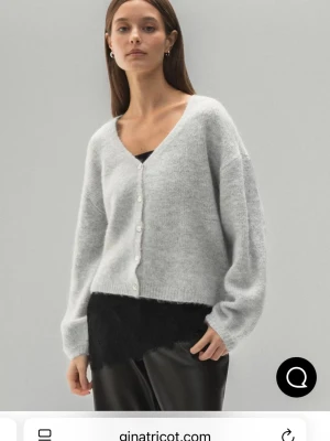 Ljusgrå kofta från Gina Tricot - Supermjuk ljusgrå kofta från Gina Tricot med v-ringning och knappar framtill. Koftan har en loose passform och är stickad i ett fluffigt material som känns riktigt cozy. Perfekt att slänga på sig över ett linne eller t-shirt.