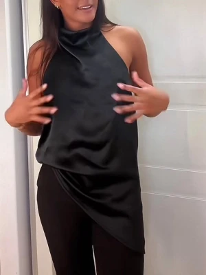 Svart halterneck topp i satin - Säljer en svart halterneck topp i glansigt satinliknande material. Toppen är ärmlös med hög krage och öppen rygg, samt har en asymmetrisk nederkant som ger en cool look. Perfekt för dig som gillar stilrena och trendiga plagg.