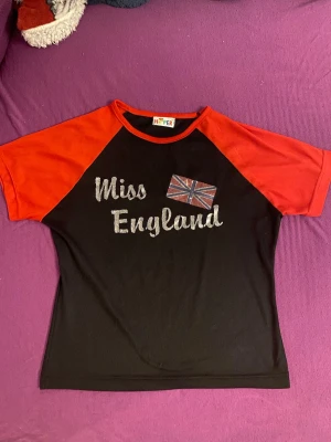 Svart och röd Miss England t-shirt - Cool t-shirt som är svart och röd och står Miss England på den. Ingen strl står men gissar på S eller Xs då personen på bilden är Xs