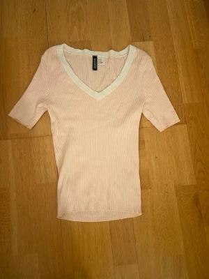 Ljusrosa ribbad topp från H&M Divided - Säljer en ljusrosa ribbad topp från H&M Divided i storlek XS. Toppen har v-ringning med vit kant och korta ärmar.
