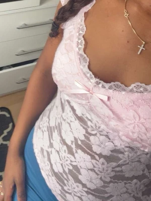 Rosa spetsblus med rosett - Söt och feminin rosa blus i spets med blommigt mönster och liten rosett framtill. Blusen är ärmlös och har en djup v-ringning med spetskant. Perfekt för dig som gillar romantisk stil. Jag själv brukar använda den som pyjamas men är egentligen inte det 