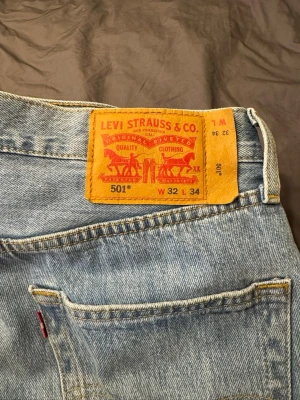 Levi's 501 ljusblå jeans W32 L34 - Klassiska Levi's 501 jeans i ljusblå tvätt med raka ben och normal passform. Jeansen har fem fickor, knappgylf och den ikoniska läderpatchen bak i midjan. Perfekta för dig som gillar tidlös stil och äkta denim.