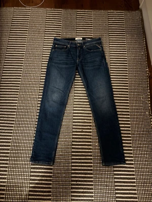 Replay Anbass mörkblå jeans - Säljer ett par Replay willby jeans i mörkblå tvätt med klassisk femficksdesign och snygga detaljer på bakfickorna. Jeansen har slim/straight passform och är tillverkade i stretchig bomull för skön komfort. Perfekt för dig som gillar stilrena och moderna jeans.