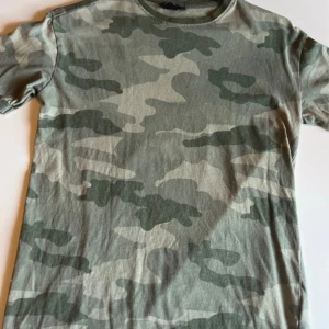 Camouflage t-shirt  - Snygg t-shirt från 157 med klassiskt camouflage-mönster i olika gröna toner. T-shirten har rund halsringning och korta ärmar, perfekt för en chill och avslappnad stil. Tillverkad i mjuk bomull som är skön att ha på sig hela dagen.