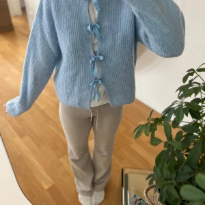 Ljusblå stickad kofta med rosetter - Superfin ljusblå stickad kofta med fyra söta rosetter framtill. Koftan har en loose passform och långa ärmar, perfekt för lager på lager. Mjuk och mysig, passar perfekt till både jeans och kjol.