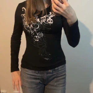 Svart långärmad topp med tryck - Svart långärmad topp med vitt och grått tryck framtill. Så sitter den på min syster men på mig är den kortare, som en lite längre magtröja. 