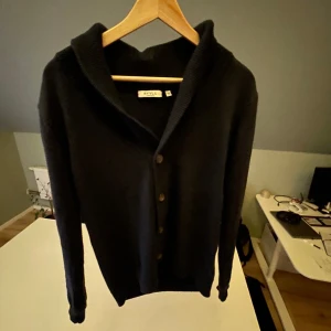 Mörkblå kofta (cardigan) från RYVLS Stockholm - Mörkblå kofta från RYVLS Stockholm med snygg, bred krage och knäppning framtill. Långärmad och i mjukt stickat material, perfekt för lager-på-lager. Enkel och stilren design som funkar till många outfits. Skulle säga att den passar någon mellan 170-180. 