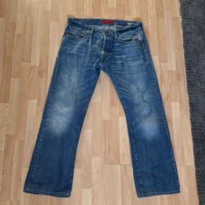 Replay Billstrong jeans blå 33/32 - Säljer ett par Replay Billstrong jeans i klassisk blå tvätt med snyggt slitna detaljer. Jeansen har raka ben, fem fickor och tydliga Replay-detaljer. Perfekt för dig som gillar en avslappnad och tidlös look.