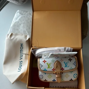 multicolor kuvertväska - Säljer en ikonisk kuvertväska  i vitt skinn med färgglatt monogrammönster. Väskan har beige läderdetaljer och ett snyggt spänne framtill. Perfekt för dig som vill sticka ut med en klassisk men lekfull accessoar.