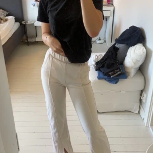 Vita vida byxor med slits framtill - Säljer ett par vita byxor med hög midja och vida ben. Byxorna har resår i midjan för extra komfort och en snygg slits framtill på benen. Perfekta för en clean och trendig look. Materialet känns mjukt och följsamt. Storlek är xxs men jag är S och dom passar perfekt! Men lite genomskinliga beroende på färg av underkläderna🥰