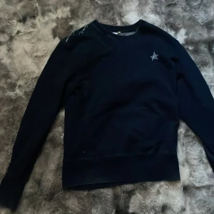 Mörkblå sweatshirt från Levi's - Mörkblå sweatshirt från Levi's med vit stjärndetalj framtill och coolt handskrivet tryck över axeln och ryggen. Klassisk passform med långa ärmar och ribbade muddar. Perfekt för dig som gillar streetstyle och vill ha något unikt i garderoben.