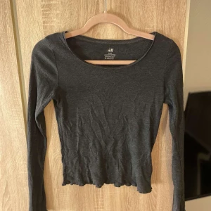 Svart ribbad långärmad tröja H&M - Mörkblå långärmad tröja från H&M Basic, tillverkad i ekologisk bomull. Tröjan har ribbad struktur, rund halsringning och en något croppad passform med vågig kant nedtill. Perfekt för dig som gillar enkel och stilren look.