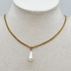 Guldfärgat halsband med pärldroppe - Stilrent halsband med en kedja i guldfärg och en droppformad vit pärla som hänge. Kedjan har klassisk länkdesign och pärlan ger en elegant touch. Perfekt för dig som gillar tidlösa smycken med en modern twist.