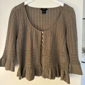 Mörkgrön kofta med volang från Lindex - Supersöt trendig grön kofta från Lindex med volangdetaljer vid ärmslut och nederkant. Koftan funkar perfekt att använda som en topp alternativt en kofta över ett plagg. Storlek M men sitter perfekt på mig som vanligtvis bär xs-s