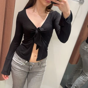 Svart croppad knytblus - Svart långärmad croppad blus med v-ringning och knyt framtill. Från ginatricot.
