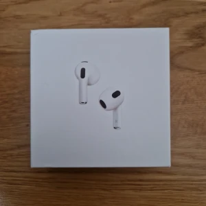 AirPods 3 - Snygga och moderna Apple AirPods 3 i originalförpackning. Trådlösa hörlurar med laddningsetui, perfekt för musik, samtal och träning. Produkten ser ut att vara i nyskick utan synligt slitage eller defekter. Levereras komplett med box och laddningsetui.