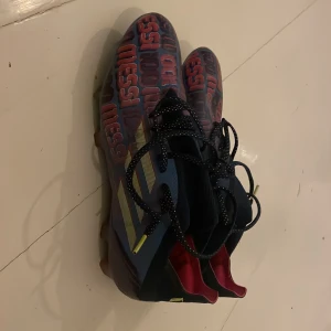 Adidas  fotbollsskor blå/lila - Säljer ett par Adidas fotbollsskor med Messi-tryck i lila över hela ovandelen. Skorna är blå med lila detaljer och svarta snören med vita prickar. Insidan är lilaoch skon har en smal, sportig form. Perfekta för dig som vill sticka ut på planen. Pris går att diskuteras