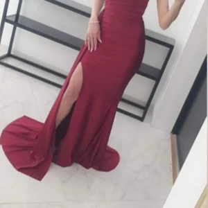 Vinröd långklänning med slits - Supersnygg vinröd långklänning med figurnära passform och hög slits på ena sidan. Klänningen har en elegant och stilren design som verkligen framhäver siluetten. Perfekt för dig som vill sticka ut och känna dig extra glam.