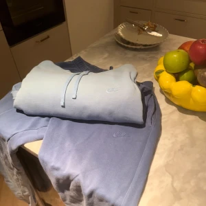 Nike hoodie + byxor SET Ombre Färg - Nike hoodie i snygg ljusblå ombre med dragsko i huvan och broderad logga på bröstet. Mjuk och skön bomull, perfekt för chill dagar. Klassisk passform och stilren look som funkar året runt. Jag lägger även in byxorna så det blir ett komplett set för dig. Hoodien är storlek Large och byxorna är medium! Använt ett par gånger endast….. Kan vara nån liten skavank, men inget märkvärdigt.