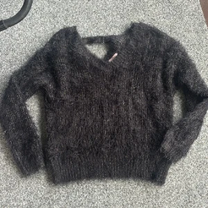 Svart fluffig stickad tröja Sincerely Loved - Mysig svart stickad tröja från Sincerely Loved i storlek S. Tröjan är fluffig med glittriga inslag och har v-ringad hals samt långa ärmar. Perfekt för dig som vill ha en trendig och bekväm look under kyligare dagar.