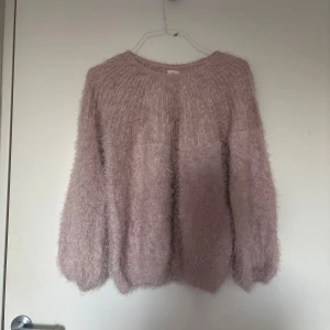 Ljusrosa fluffig stickad tröja - Supermjuk och fluffig stickad tröja i ljusrosa färg. Tröjan har rund halsringning och långa ärmar, perfekt för att hålla sig varm och mysig under kyliga dagar. Den har en avslappnad passform och är riktigt skön att bära.