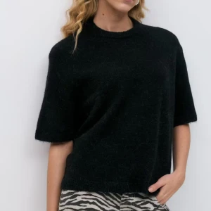 Svart stickad tröja med kort ärm - En svart stickad tröja med avslappnad passform och korta ärmar. Tröjan har rund halsringning och är perfekt för lager-på-lager. Enkel och stilren design som funkar till många outfits.