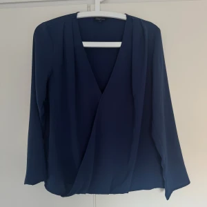 Marinblå blus från Xoul Edition - Snygg marinblå blus från Xoul Edition i storlek S. Blusen har långärmade ärmar och djup v-ringning framtill. Tillverkad i ett lätt och mjukt polyestertyg som ger ett elegant fall. Perfekt för dig som gillar stilrena och enkla plagg.