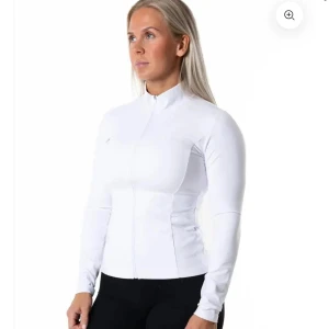 Vit vindjacka med dragkedja - Snygg vit vindjacka med hel dragkedja framtill och hög krage. Jackan har en slim passform och är tillverkad i ett syntetmaterial som känns lätt och smidigt. Perfekt för dig som gillar sportig stil och vill ha en jacka som sitter tajt och bekvämt.