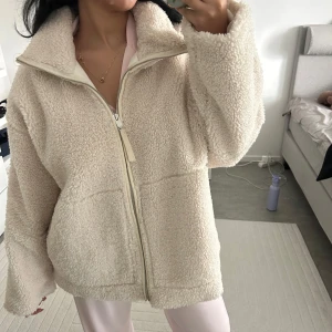Beige teddyjacka med dragkedja - Supermjuk och oversized teddyjacka i beige med hög krage och hel dragkedja framtill. Jackan har stora fickor och är tillverkad i fluffigt fleece-material som håller dig varm och cozy. Jackan är i storlek 42 men passar mig som bär 38 super bra.