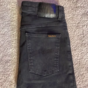 Svarta skinny jeans från Nudie Jeans - Svarta skinny jeans från Nudie Jeans med klassisk femficksdesign och diskret logga på bakfickan. Jeansen har smal passform och är tillverkade i stretchigt bomullsmaterial för en bekväm känsla. Perfekta för dig som gillar en stilren och modern look.